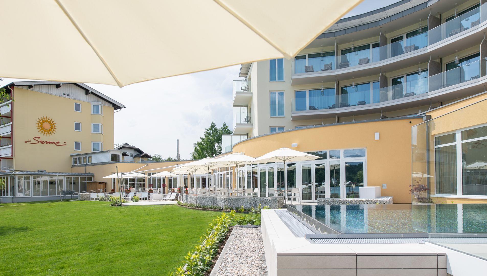 Sonnenwiese und Pool mit Schirmen vor Hotelgebäude