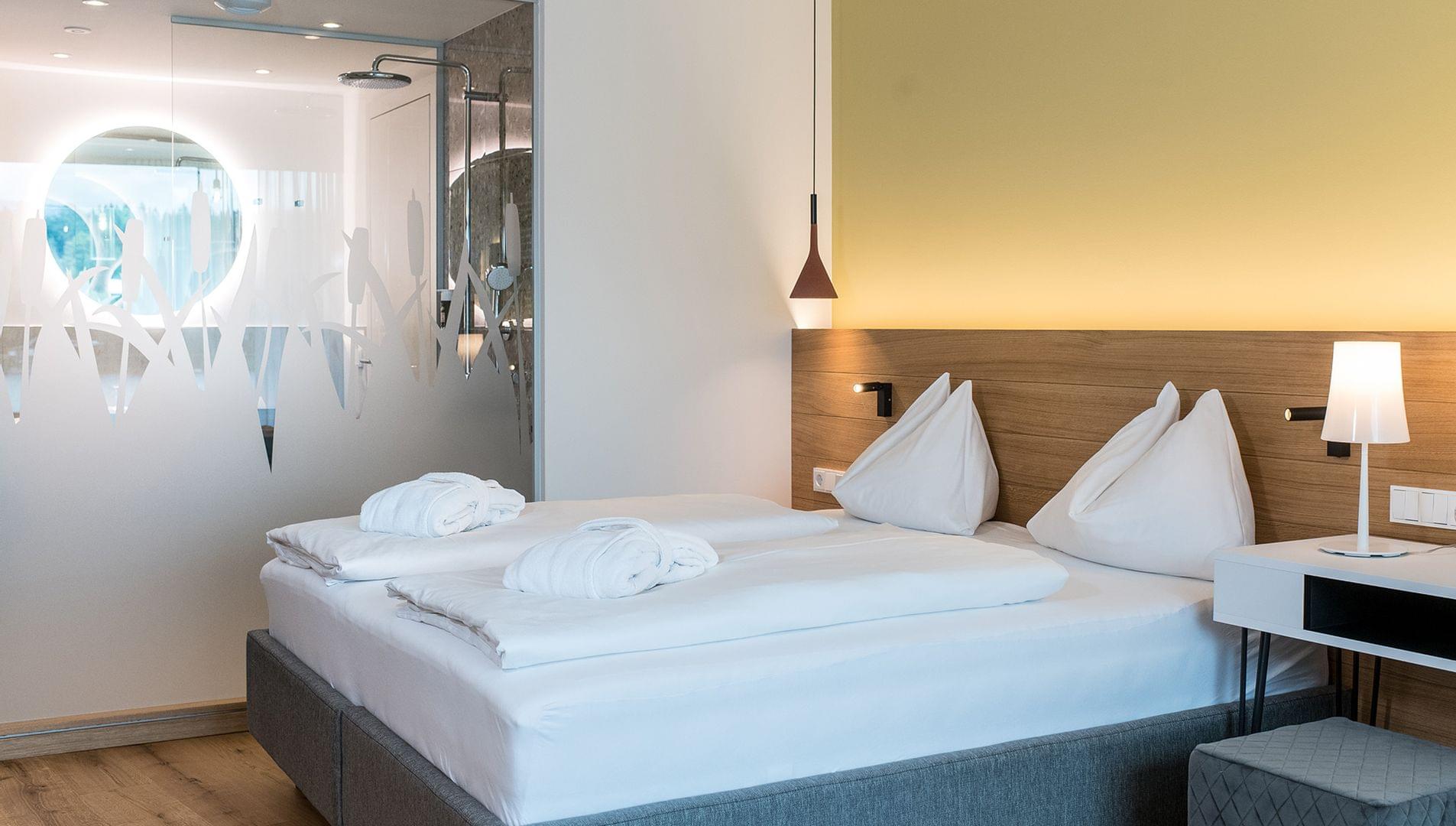 Doppelbett vor Milchglas mit Blick ins Bad